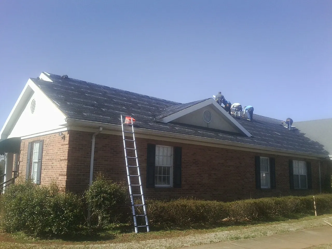Crew tearing shingles off a brick ranch roof with a ladder set — Metal Roof Repair work by our crew in Mekinock