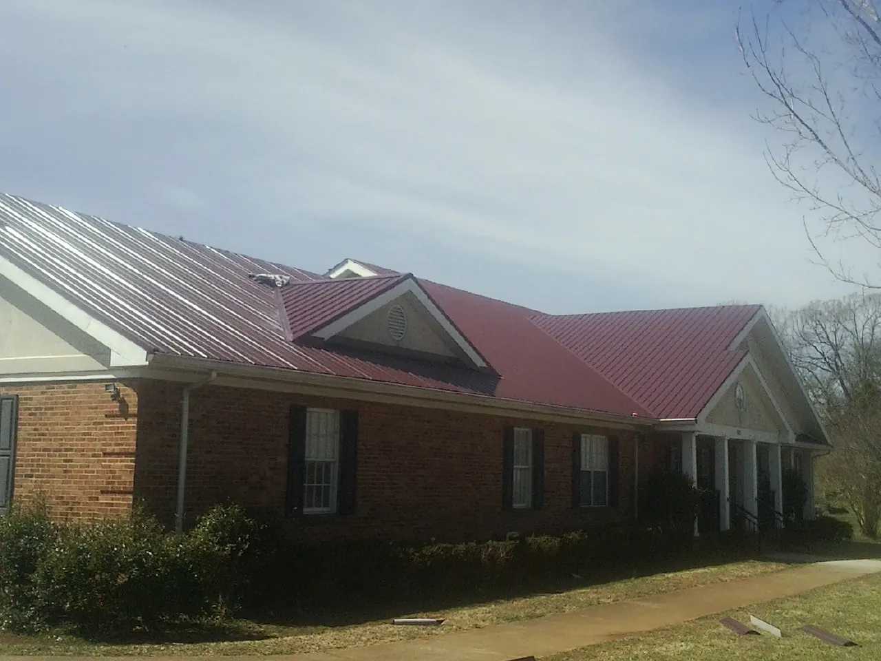 Red metal roof with gabled entries on a long brick building, from a Hail Damage Roof Repair job in Mekinock