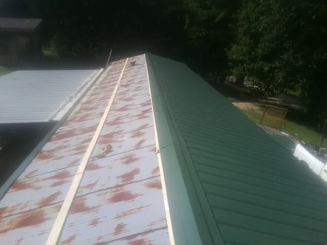 Old rusted panels beside newly installed green metal roofing — Wind Damage Roof Repair by Roofing Brothers in Mekinock