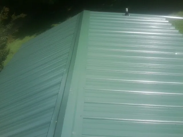 New green metal panels meeting at the ridge of a roof — Flat Roof Repair work by our crew in Mekinock