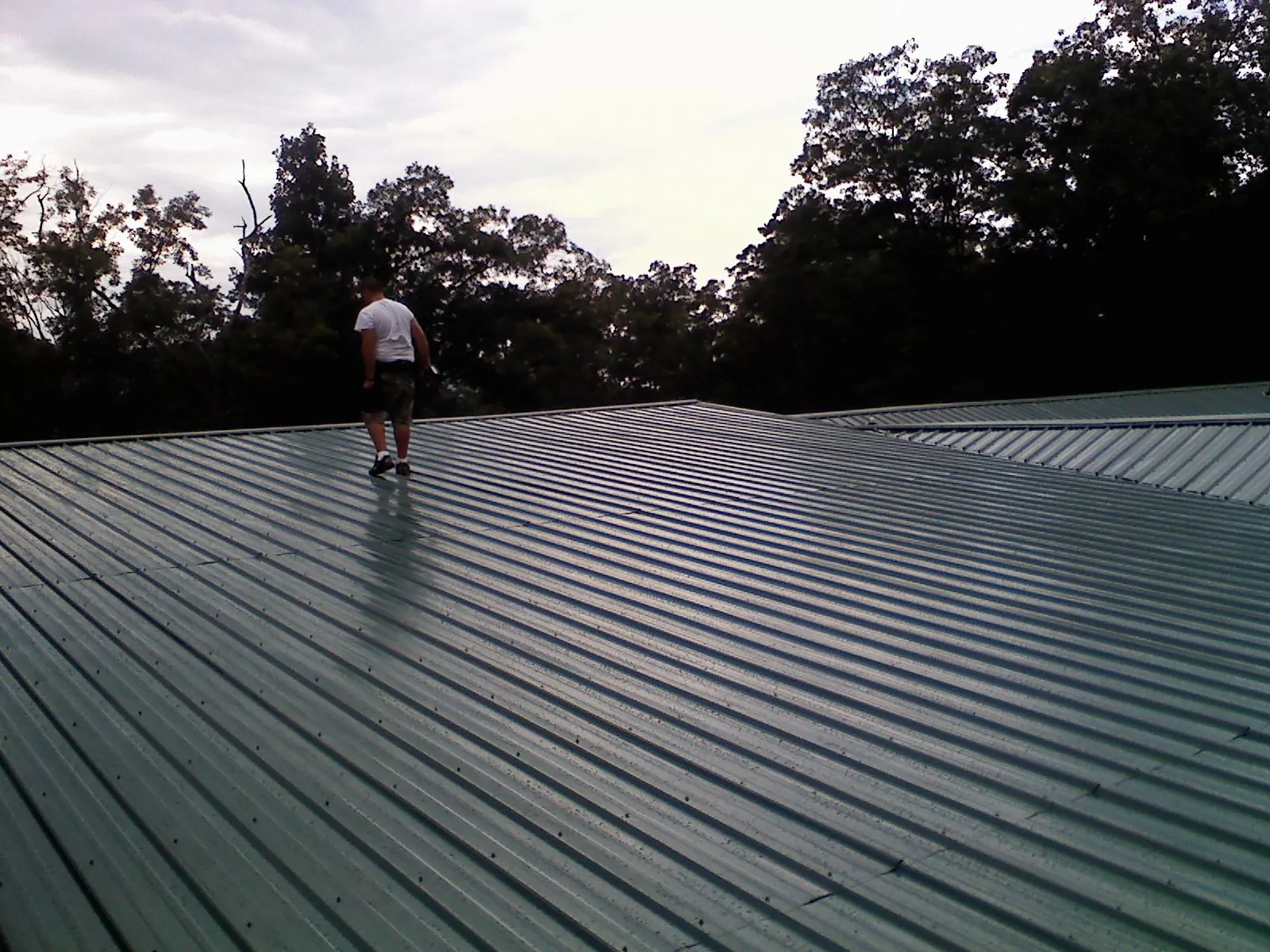 Roofer walking a wide expanse of new green metal roofing in Mekinock