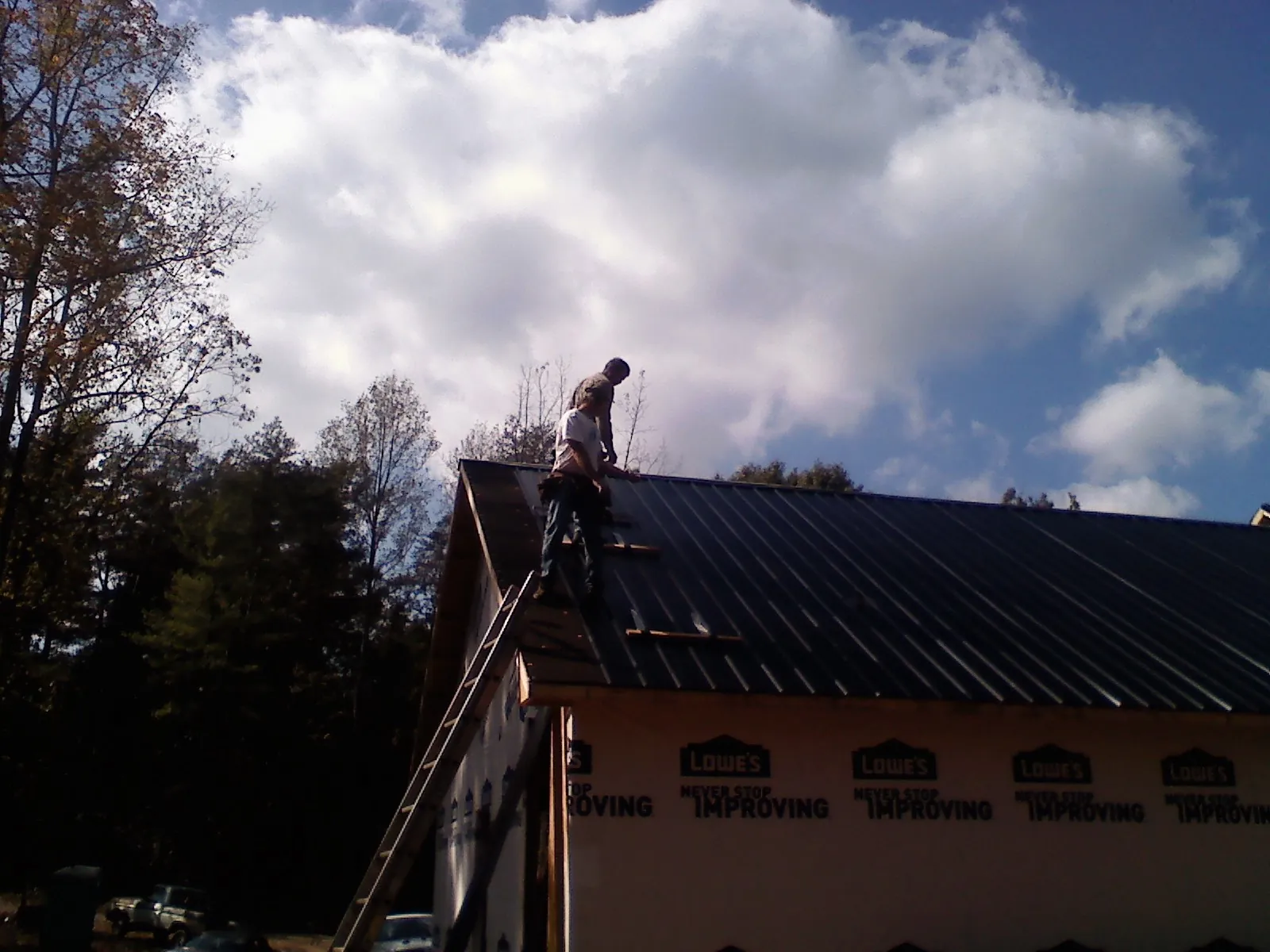 Roofer fastening dark metal panels high against a cloudy sky, from a Roof Inspection job in Mekinock