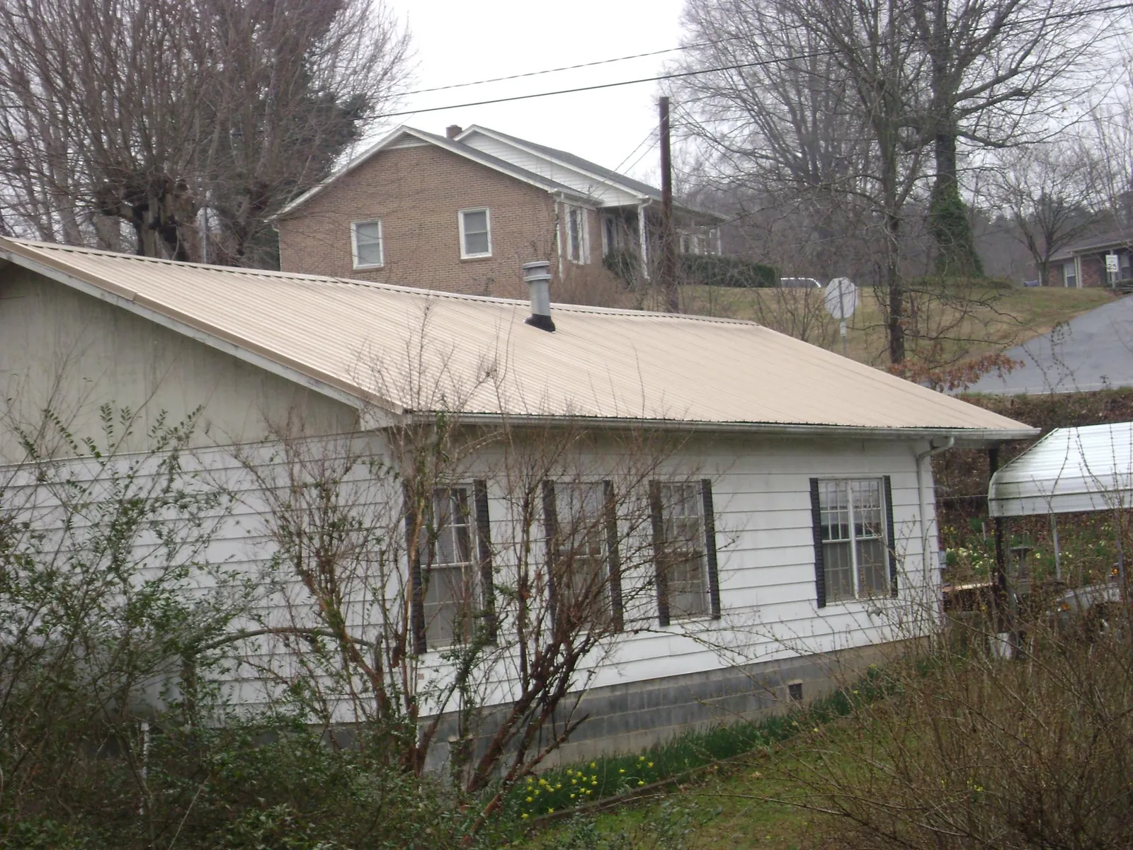 Tan metal roof on a white sided house set into a hillside — Commercial Roofing by Roofing Brothers in Mekinock